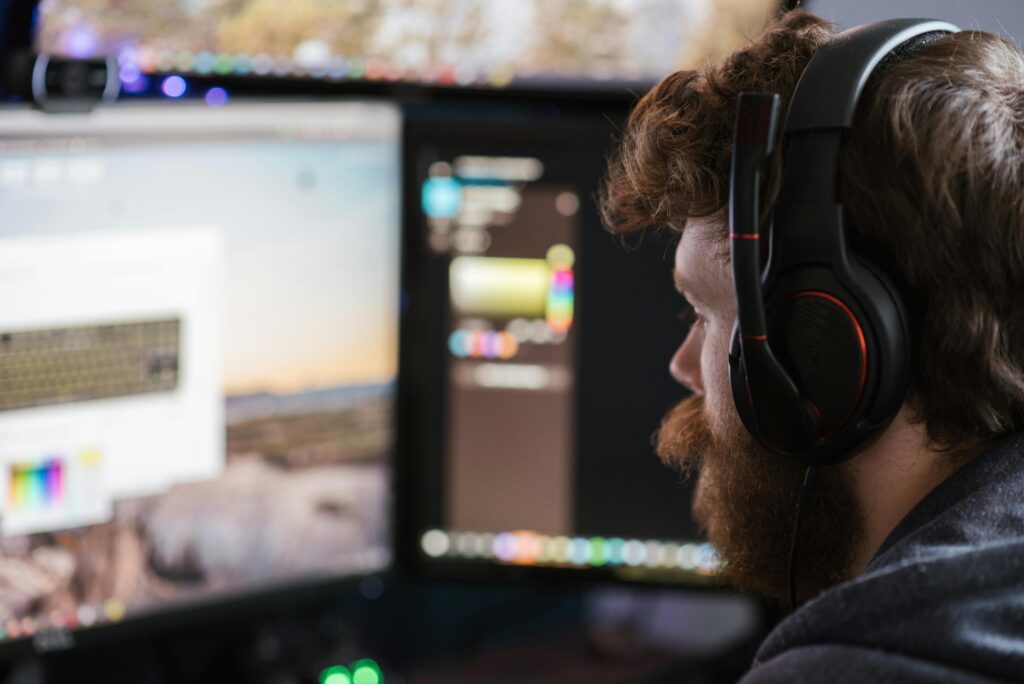 Man with headset concentrating on work at dual monitors in a home office setting.